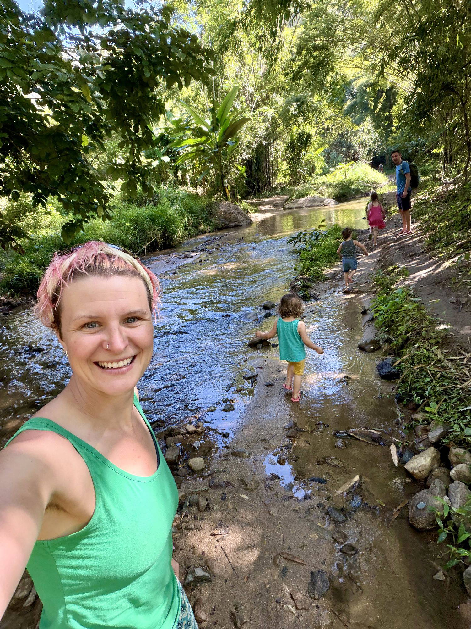Anna McNuff smiling by a jungle stream while her children and partner explore behind her